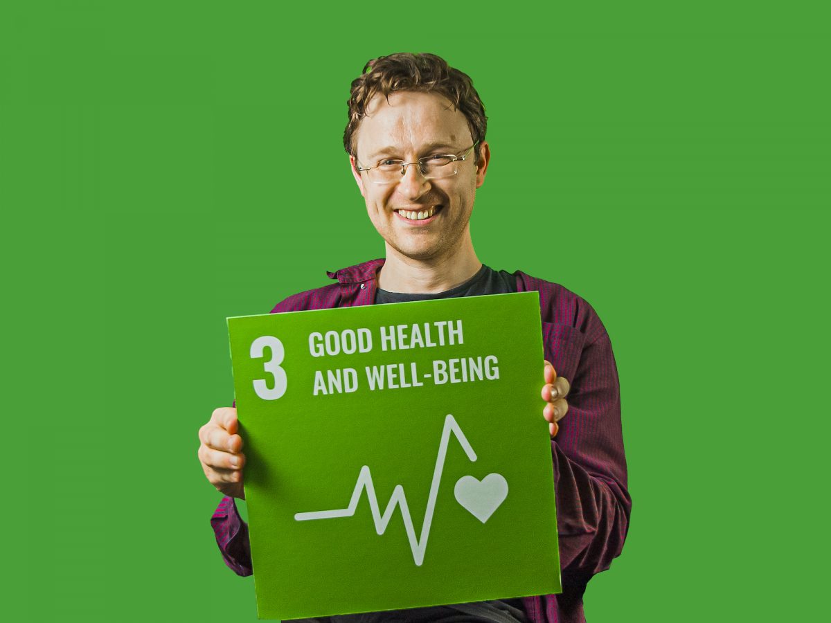Man holding up sign showing Global Sustainable Development Goal 3, good health and well-being.